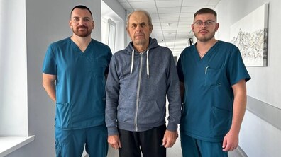 У холі лікарні стоять зліва на право: лікар-хірург Даниїл Плахтина, пацієнт Степан та лікар-хірург Тарас Дем'янович. Усі троє дивляться в камеру.