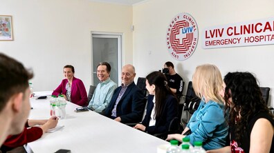Робоча зустріч у конференц-залі лікарні святого Пантелеймона (на стіні є логотип Lviv Clinical Emergency Hospital). За великим столом сидять учасники розмови: вони щось обговорюють, частина з них усміхається.