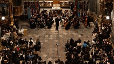 Більше десятка учасників оркестру INSO-Львів грають на музичних інструментах перед вівтарем в Гарнізонному храмі. Довкола багато людей спостерігають, слухають музику та знімають на телефон