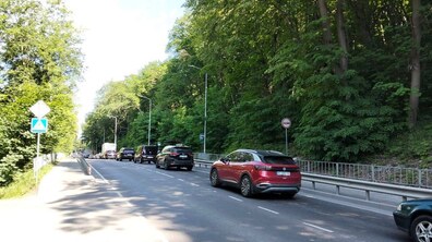 Автівки їдуть вулицею, з обох боків видно зелені дерева