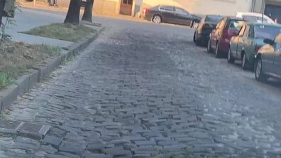 Нерівна брукована вулиця, на якій припарковані автомобілі.