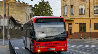 Червоно-сірий низькопідлоговий автобус №48 курсує вулицею Львова. На другому плані видно історичну забудову та дерево, на тротуарі стоїть зелений електросамокат