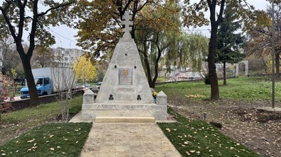 Кам’яний пам’ятник у формі піраміди з хрестом на верхівці, розташований у сквері серед осінніх дерев. На монументі видно український герб та пам'ятний напис.