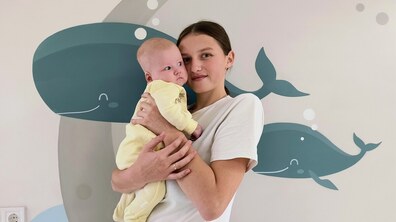 Мама Марія тримає на руках свою донечку Кароліну, на задньому фоні – лікарняна стіна з рибками