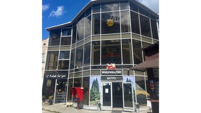 Велика триповерхова скляна будівля з вивіскою та написом «Фабрика їжі. Бістро». Зліва – Кебаб. На другому поверсі на екрані напис – «Піца». Біля споруди ще один невеликий кіоск