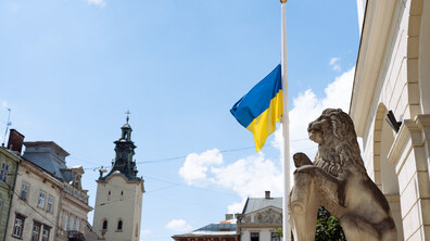 Приспущений синьо-жовтий прапор майорить на флагштоці перед будівлею Львівської міської ради. Праворуч розташована велика кам’яна скульптура лева, позаду - міські будівлі.