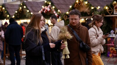 Дівчина та хлопець на фоні Різдвяного ярмарку, тримають в руках різдвяний дідух