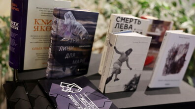На темному столі розставлені сучасні українські видання, що були представлені на премії Львова — міста літератури ЮНЕСКО. Серед них виділяється книга Сергія Осоки «Три лини для Марії» з ілюстрацією риби на обкладинці та книга Ірини Шувалової «Каміньсадліс». Перед книжками лежать інформаційні буклети премії з геометричним фіолетовим візерунком