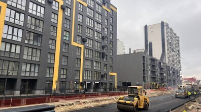 Техніка прокладає новий асфальт. Позаду сучасні багатоповерхівки.