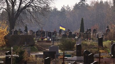Голосківське кладовище восени. На фото видно численні надгробки та хрести серед пожовклої трави й дерев. У центрі майорить синьо-жовтий прапор України. На задньому плані простягається ліс.