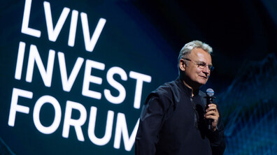 Міський голова з мікрофоном у руках виступає на форумі. Позаду нього видніється великий екран з назвою події