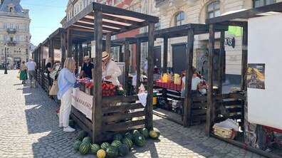 На площі Ринок розташовані дерев’яні торгові ятки фермерського ярмарку, де люди купують овочі, фрукти та інші продукти