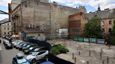 Площа Нижанківського у центрі Львова. На передньому плані припарковані автомобілі, а за огорожею видно велику бетоновану ділянку з металевою арматурою. Навколо простору розташовані старі кам’яниці, а на стінах сусідніх будівель помітні графіті.