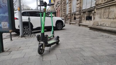 Електросамокати на тротуарі. На задньому плані видно автомобіль. Фото ілюстративне.