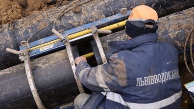 траншея у якій прокладено два паралельних поліетиленових трубопроводи. На нижньому трубопроводі встановлена спеціальна металева конструкція, за допомогою якої працівник Львівводоканалу проводить з’єднання труб між собою.
