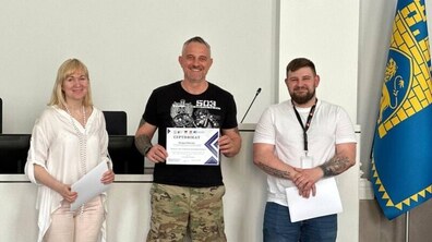На фото зображено учасника “Відвага до бізнесу” із сертифікатом про закінчення програми. Поруч з ним представник організаторів та очільниця департаменту економічного розвитку Львівської міської ради Інна Свистун
