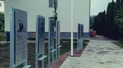 Простір пам’яті зі стендами, на яких розміщено портрети та біографії загиблих українських воїнів. На другому плані видно світлу будівлю та зелені дерева