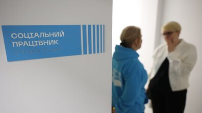 Соціальна працівниця спілкується з людиною, на фоні табличка «Соціальний працівник»