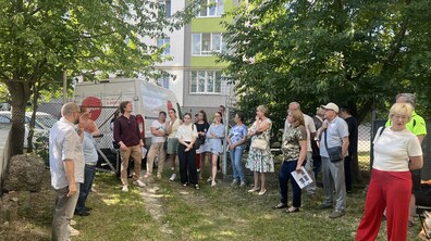 Мешканці та представники міста під час виїзної зустрічі на вул. Драгана. Учасники стояють біля багатоповерхівки і розглядають будівлю поряд