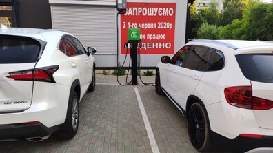 Два автомобілі білого кольору припарковані біля зарядної станції.