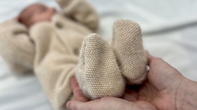 Немовля лежить на ліжку, його ніжки тримають руки дорослої людини