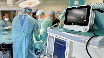 Лікарі проводять хірургічне втручання в операційній. Вони у стерильному одязі працюють біля операційного стола, над яким світить велика лампа. На передньому плані – спеціальний монітор, що показує серцеві ритми пацієнта.
