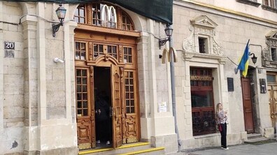 Історичний будинок в центральній частині міста з масивним різьбленими дерев’яними дверима та архітектурними елементами в класичному стилі. Біля фасаду видно державний прапор України