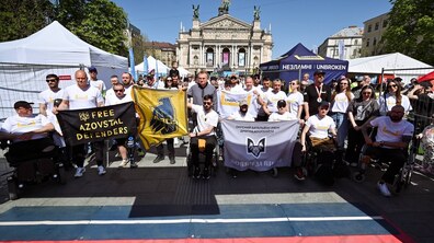 Кілька десятків ветеранів та пацієнтів центру НЕЗЛАМНІ (UNBROKEN) з міським головою Львова Андрієм Садовим на старті забігу напівмарафону. Ветерани тримають в руках прапори Азову, НЕЗЛАМНИХ, Вовків Да Вінчі та інші. Позаду видно оперний театр.