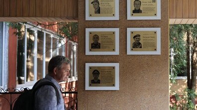 Чоловік проходить біля фасаду школи. На стіні є п'ять меморіальних таблиць полеглим захисникам. На кожній є фото Героя та коротка інформація про нього