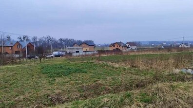 Земельна ділянка, заросла травою. На фоні позаду приватні житлові будинки та автівки