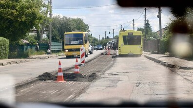 Частина вул. Шевченка, де тривають ремонтні роботи. Старий шар асфальту вже зрізали, місце ремонту огороджене помаранчевими конусами та дорожніми знаками. Назустріч один одному рухаються автобуси, а позаду них видно інші автомобілі та дорожню техніку.