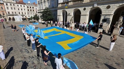 Багато людей на площі Ринок тримають великий кримськотатарський прапор – блакитний прапор із жовтою тамгою. Поруч майорять українські та кримськотатарські прапори, а поруч стоять учасники заходу.
