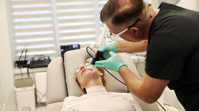 Косметологічна процедура: фахівець у чорному одязі та захисних рукавичках проводить апаратну обробку обличчя жінки, яка лежить у спеціальному кріслі.