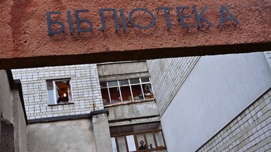 Великими літерами встановлено слово - бібліотека на стіні будинку. Позаду на фоні розбиті вікна