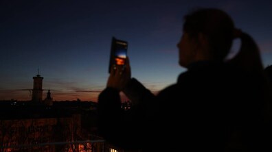 Жінка в темряві дивиться на екран мобільного телефона. Позаду неї видно Ратушу та центральну частину Львова в темряві.