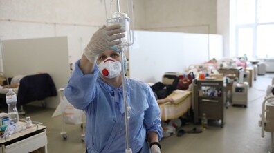 медсестра у халаті та масці ставить ліки у крапельницю, на фоні - лежачі пацієнти