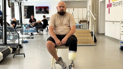 Захисник Олександр сидить у реабілітаційному залу центру UNBROKEN та уважно дивиться в камеру. У нього – протез нижньої кінцівки. Навколо видно тренажери та обладнання для фізичної терапії.