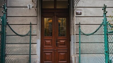 Двостулкова дерев’яна брама коричневого кольору зі скляними вставками зверху. Вона розміщена у кам'яному порталі будівлі, по обидва боки від входу встановлена зелена металева сітчаста огорожа, а праворуч на стіні висить табличка з номером «14».
