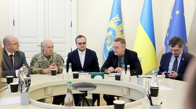 На світлині зображено частину круглого столу у світлій залі Львівської міської ради. У центрі кадру — мер Львова Андрій Садовий. По праву руку від нього сидять перший заступник Андрій Москаленко, а також ректор Національної академії сухопутних військ ім. Петра Сагайдачного у піксельній формі. На фоні за ними стоять три прапори: блакитний прапор Львова із гербом Львова, синьо-жовтий прапор України та прапор Європейського Союзу.