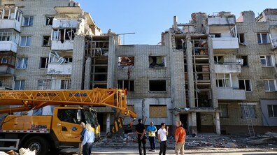 Будинок на вул. Патона, пошкоджений внаслідок ракетного удару. У центральній частині зруйновані верхні поверхи, вибиті вікна та частково обвалені стіни. Перед будинком працює автокран, а біля нього стоять люди, які оглядають хід аварійно-відновлювальних робіт.