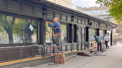 Чоловік на драбині розбирає ліхтарі в дерев’яному літньому майданчику. Позаду ще двоє працівників демонтовують дерев'яні елементи конструкції