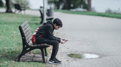 Хлопчик у сірому худі сидить на лавці в парку.