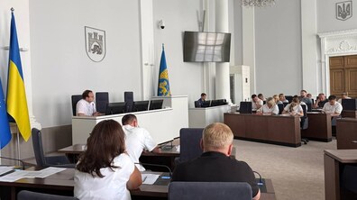 Засідання штабу з підготовки до зими у великій сесійній залі Львівської міської ради. У центрі — Андрій Москаленко за трибуною, він виступає перед присутніми. У залі за робочими столами сидять учасники наради, частина з них робить записи. Ліворуч видно державний прапор України, а поруч — прапор Львова.