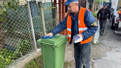 працівник Львівспецкомунтрансу клеїть наліпки з QR-кодом на бак для відходів