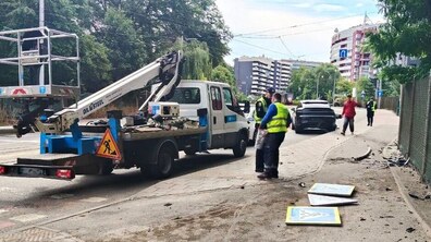 Місце ДТП, де автомобіль врізався в опору світлофора. На місці працює ремонтна бригада зі спецтехнікою, яка ліквідовує наслідки аварії та відновлює пошкоджену інфраструктуру. На тротуарі лежать дорожні знаки та уламки конструкцій.