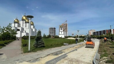 Процес облаштування нової велодоріжки на Сихові: на передньому плані видно дорожню техніку та ділянку, де вже підготували основу для майбутнього покриття і встановили бордюри. На тлі синього неба ліворуч височіє біла церква Різдва Пресвятої Богородиці. На другому плані видно багатоповерхові житлові будинки.