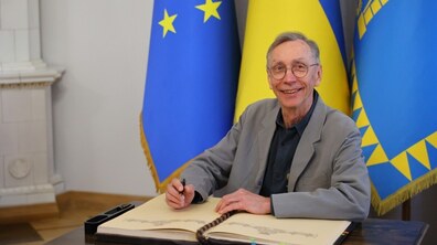Нобелівський лауреат Сванте Паабо посміхається під час запису в Книгу почесних гостей Львова. Позаду нього прапори ЄС, України та Львова.